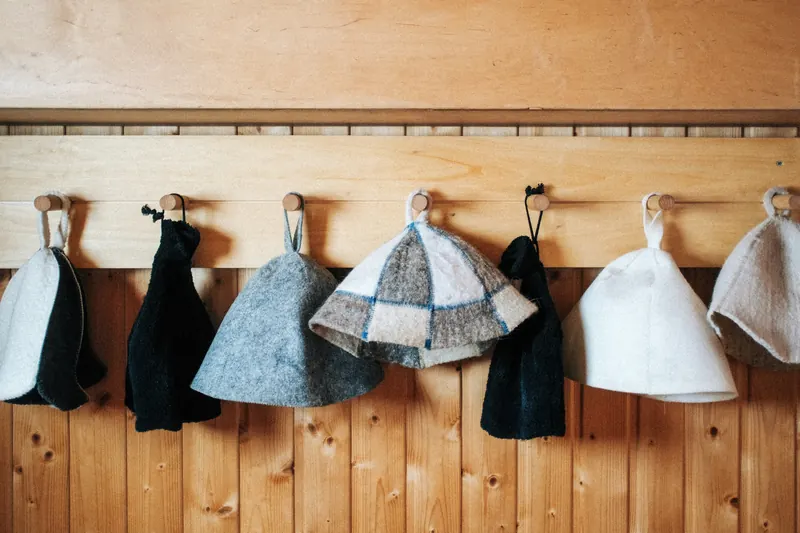 Felt and terry sauna hats hanging on wooden pegs in a dressing room